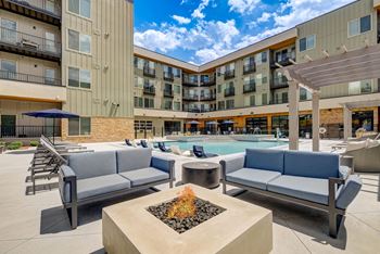 a poolside lounge area with chairs and a fire pit in front of a building